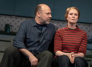 A photograph shows Danny Burstein sitting beside Cynthia Nixon in a modern kitchen set, with Burstein looking toward her as she faces forward with a pained expression during a scene from Marjorie Prime.