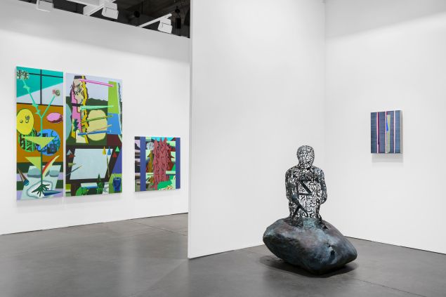 An art fair booth with white walls and a mix of paintings and sculpture