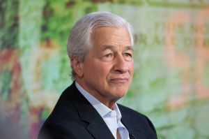 Man with grey hair and black suit pictured against green background