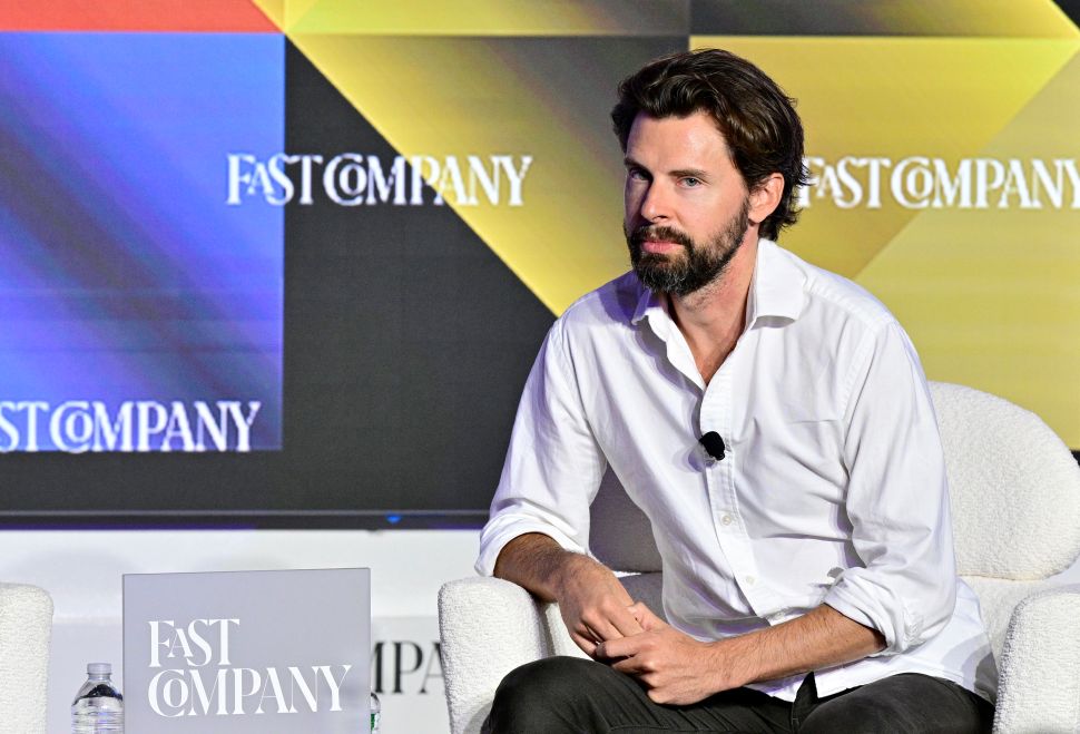 Man in white button up shirt sits in chair onstage